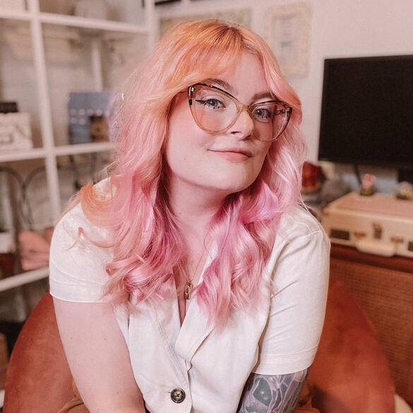 A portrait of Olivia, a white woman with pink hair and glasses.